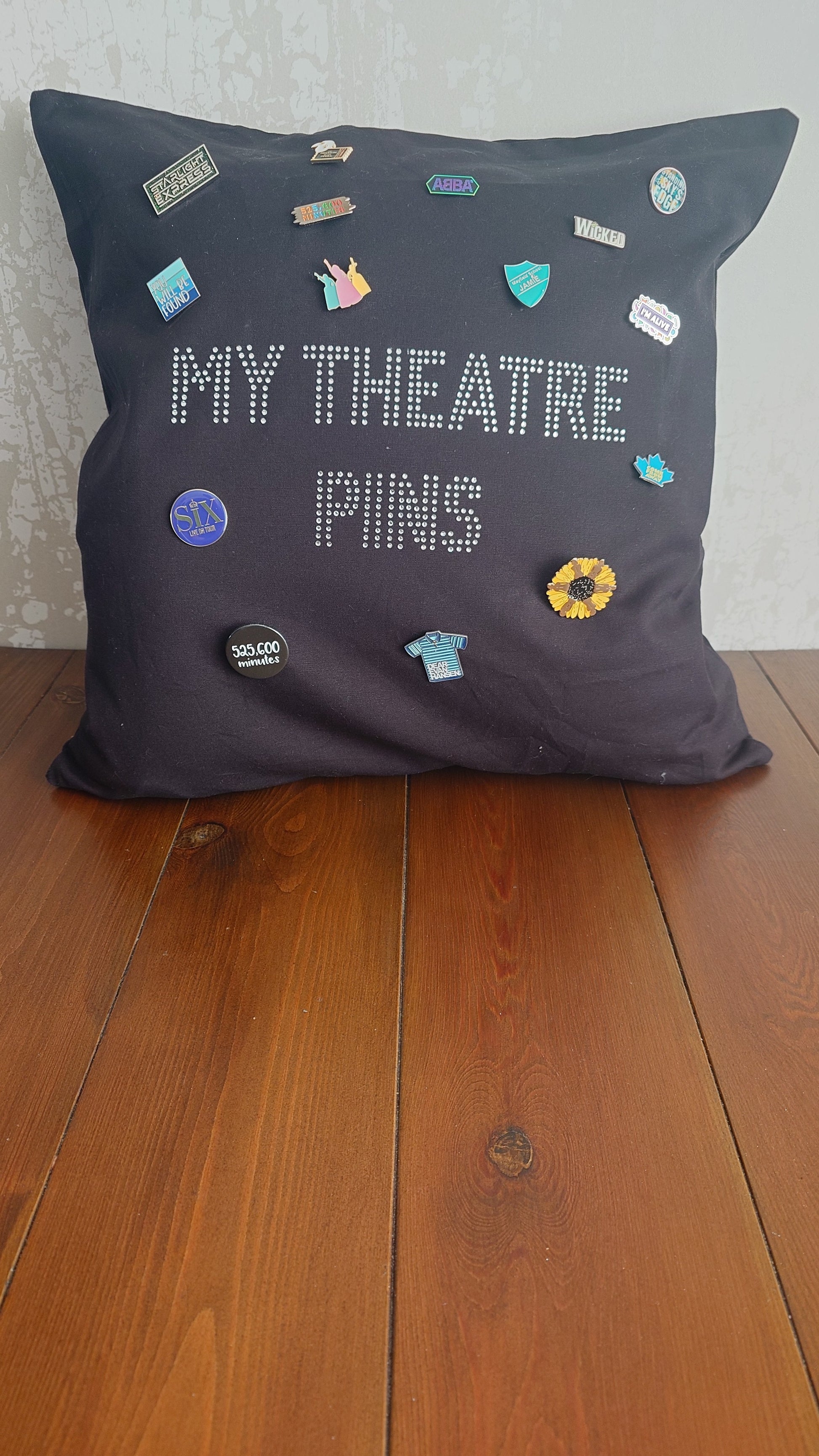 Square black cotton cushion cover with silver rhinestone writing in the middle spelling out 'MY THEATRE PINS' the cushion has lots of theatre themed pins on it to show how it can be used to display pins