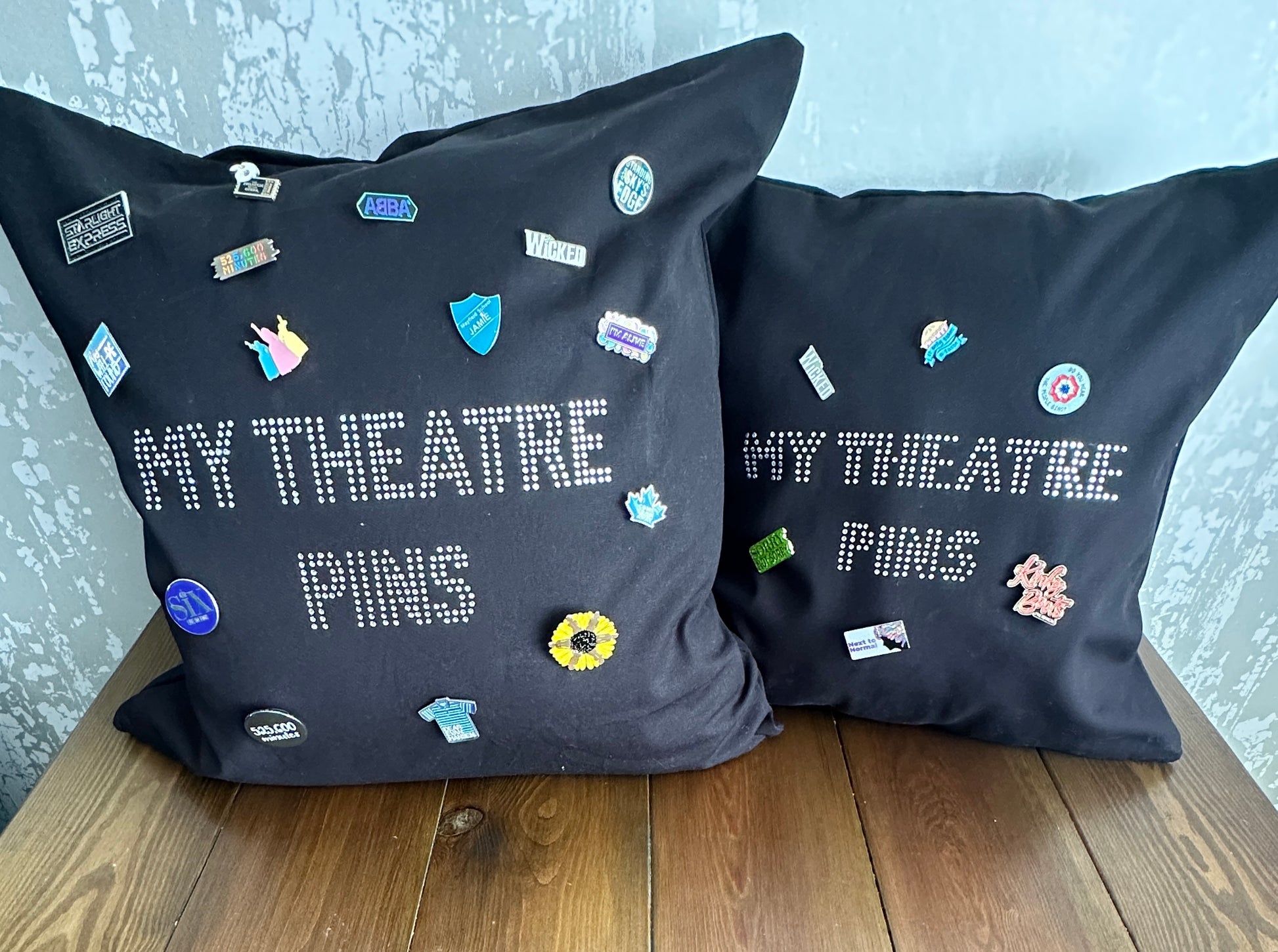 2 Square black cotton cushion cover s in two different sizes, with silver rhinestone writing in the middle spelling out 'MY THEATRE PINS' the cushion has lots of theatre themed pins on it to show how it can be used to display pins