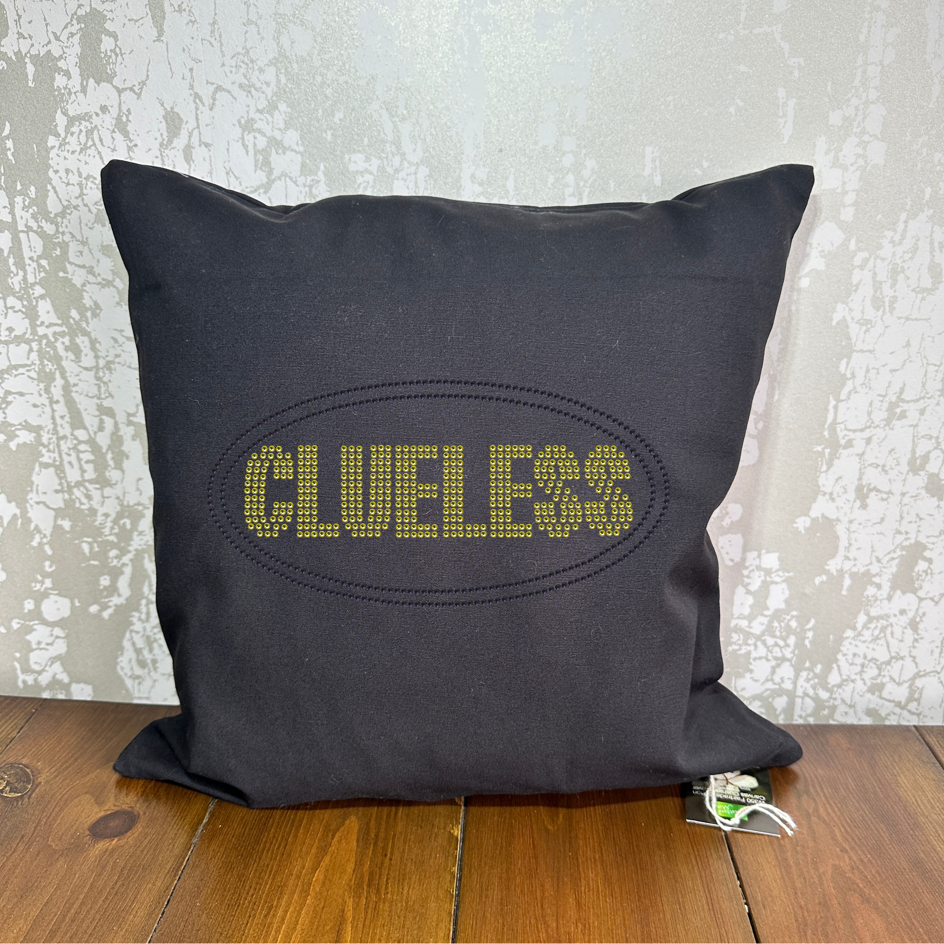 Black cotton, square cushion cover with bright yellow clueless writing in a block font, around the lettering is a black oval outline. The design is made up of sparkling rhinestones.
Design is placed on the front of the cushion,