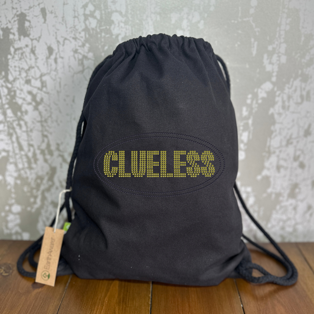 Thick cotton drawstring bag with bright yellow clueless writing in a block font, around the lettering is a black oval outline. The design is made up of sparkling rhinestones.
Design is placed on the front of the bag