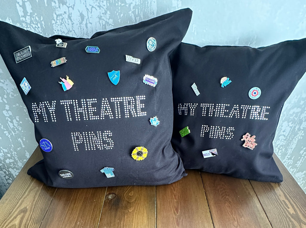 Square black cotton cushion cover with silver rhinestone writing in the middle spelling out 'MY THEATRE PINS' the cushion has lots of theatre themed pins on it to show how it can be used to display pins
